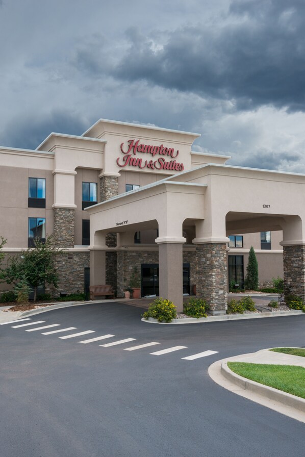 A Hampton Inn & Suites hotel with a stone facade, large windows, and a clear sky.