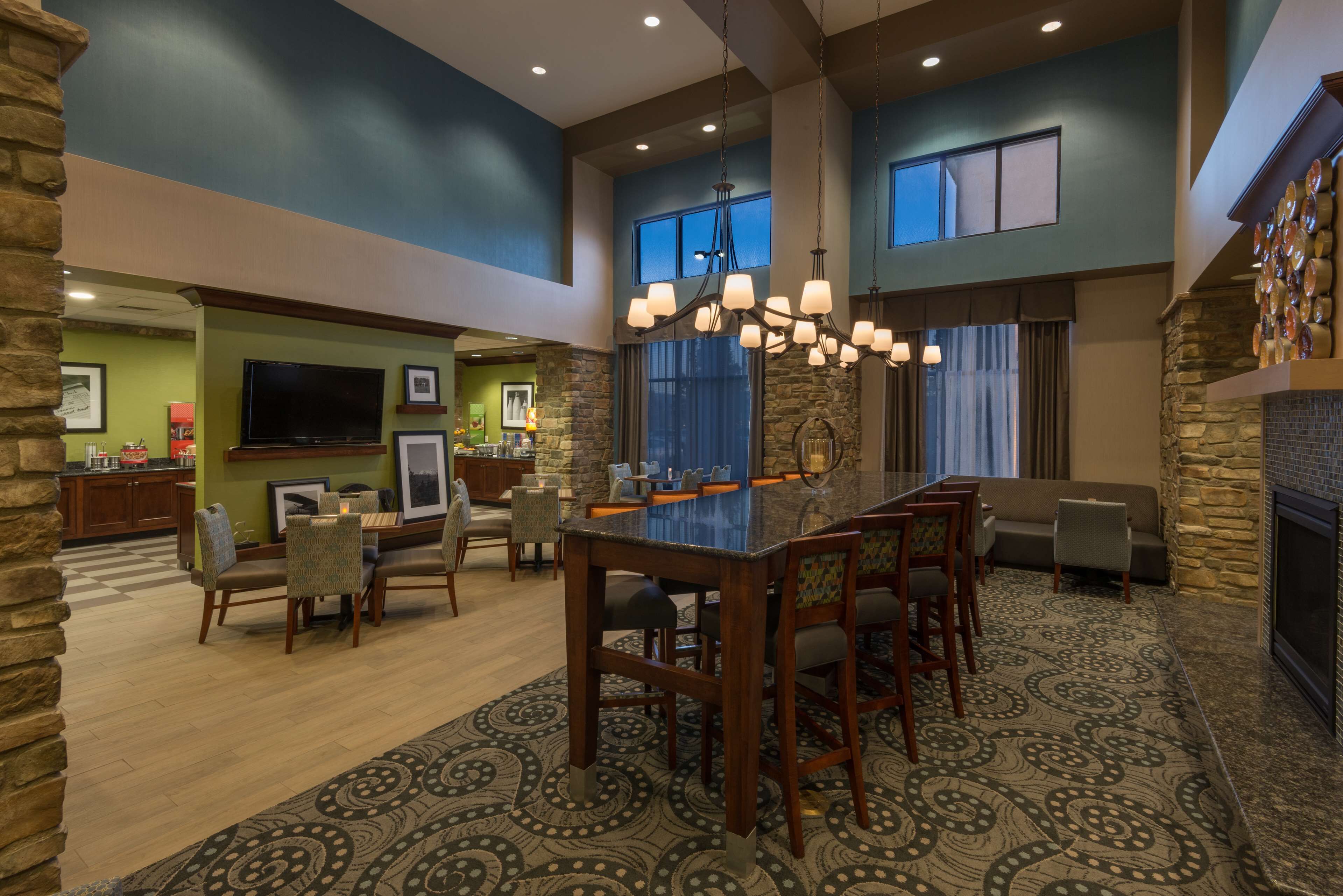 A spacious living room with a large dining table, comfortable seating, a stone fireplace, and a television.