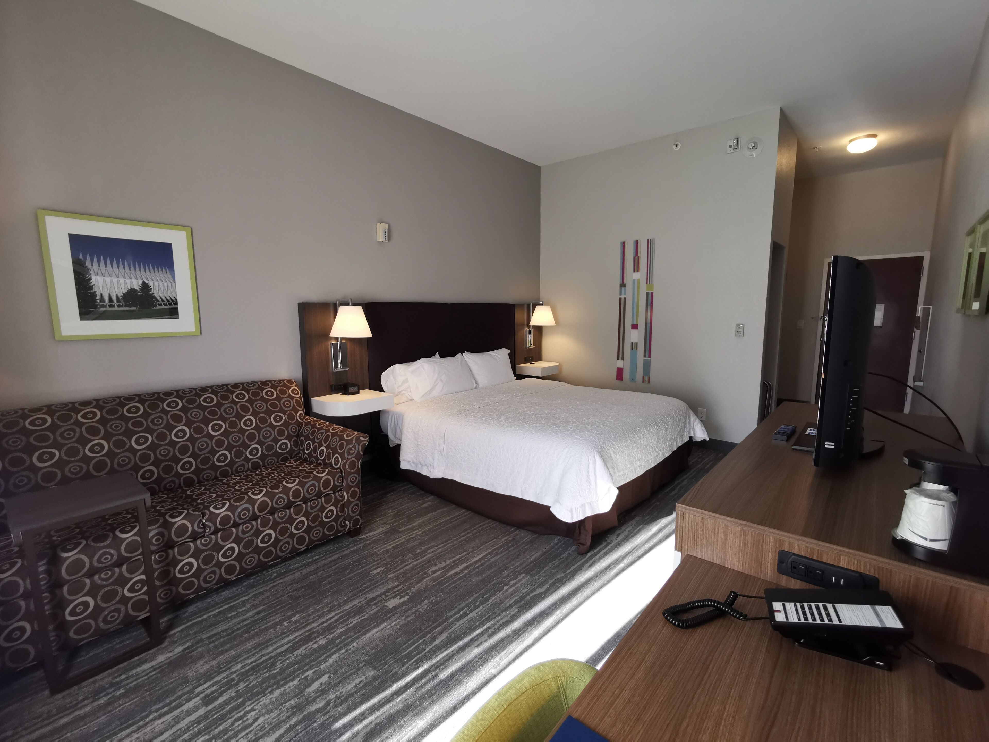 A hotel room with a bed, a sofa, a desk with a computer, and a TV.