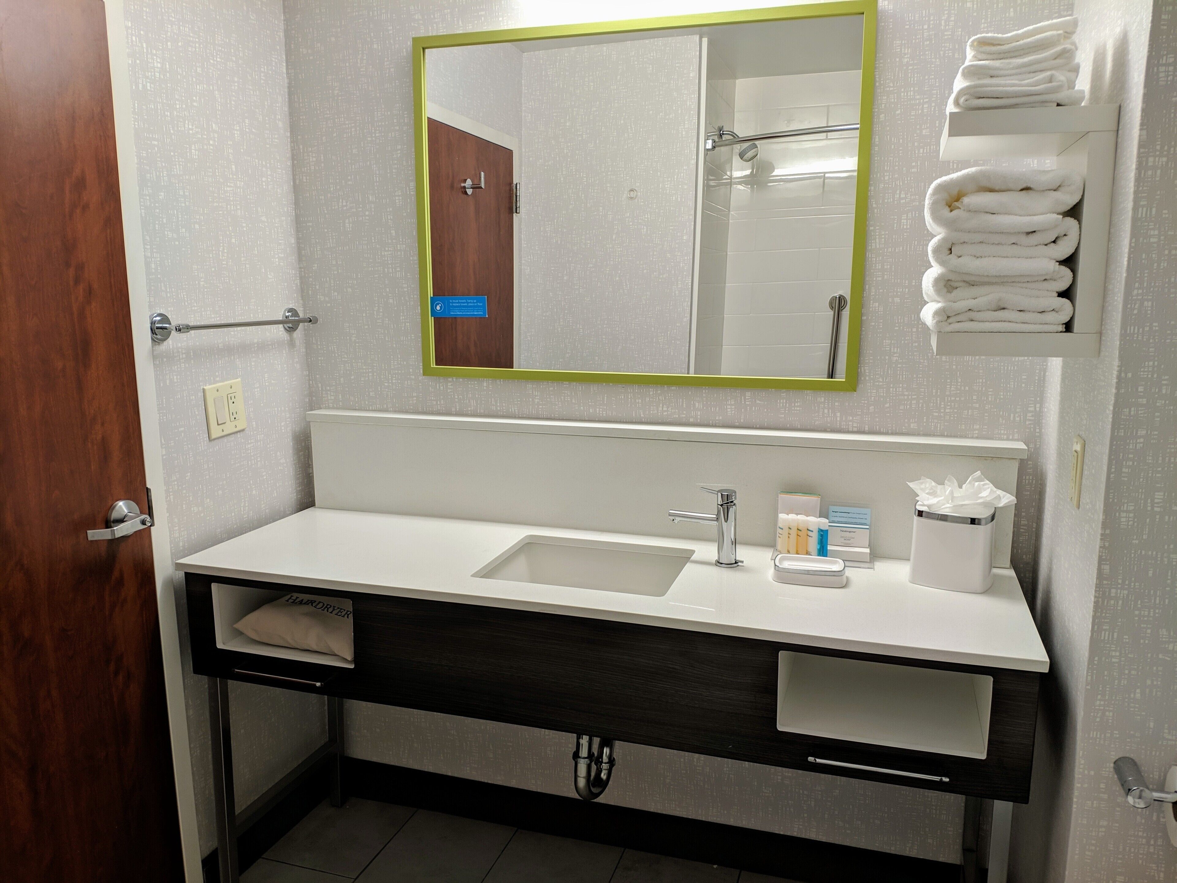 Casa de banho com lavatório branco, espelho com moldura verde e porta-toalhas com toalhas dobradas.