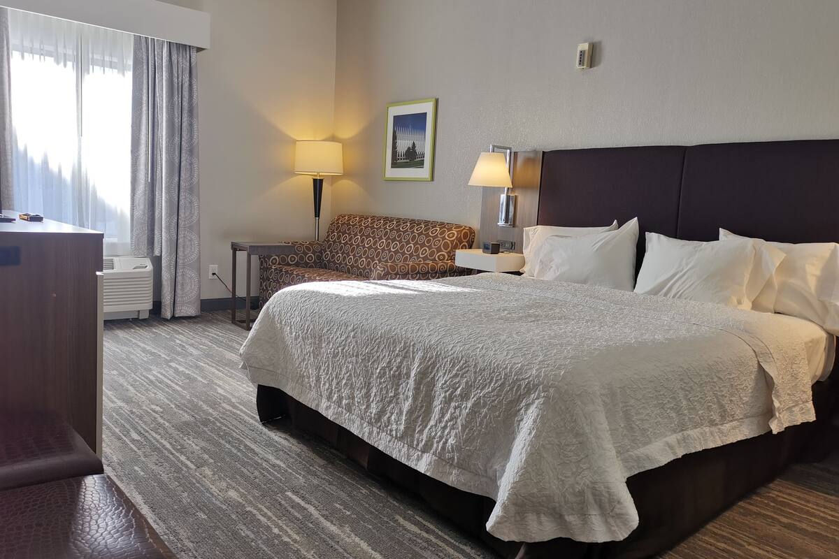 A hotel room with a large bed, a desk, a chair, and a lamp.