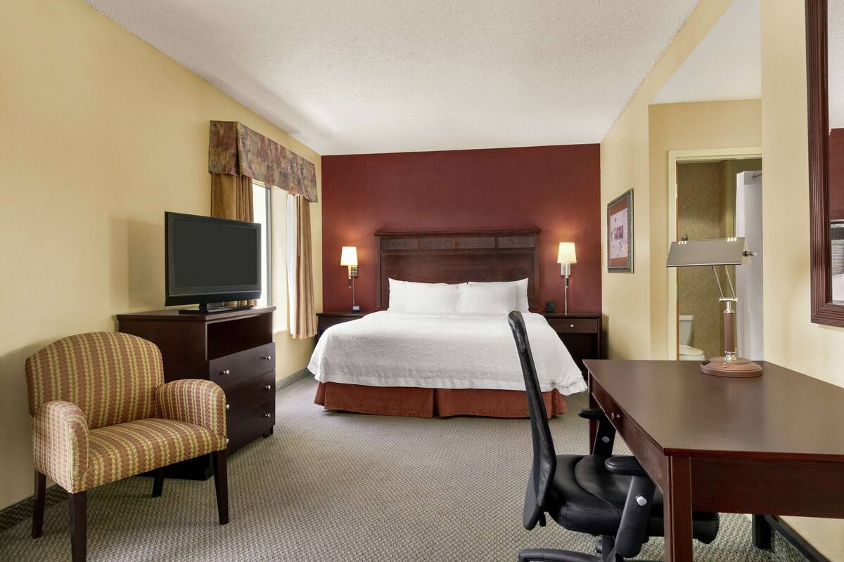 A hotel room with a bed, a desk, a chair, a television, and a lamp.