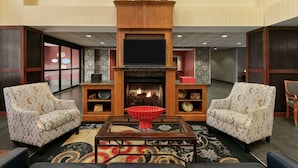 A living room with a fireplace, two patterned armchairs, a coffee table, and a decorative bowl. - Hampton Inn & Suites Lawton (Lawton)