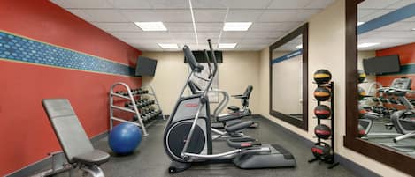 Un gimnasio con equipo de ejercicio, una banca y un espejo.