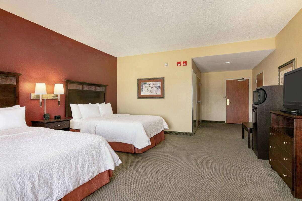 A hotel room with two beds, a TV, a desk, and a framed picture on the wall.
