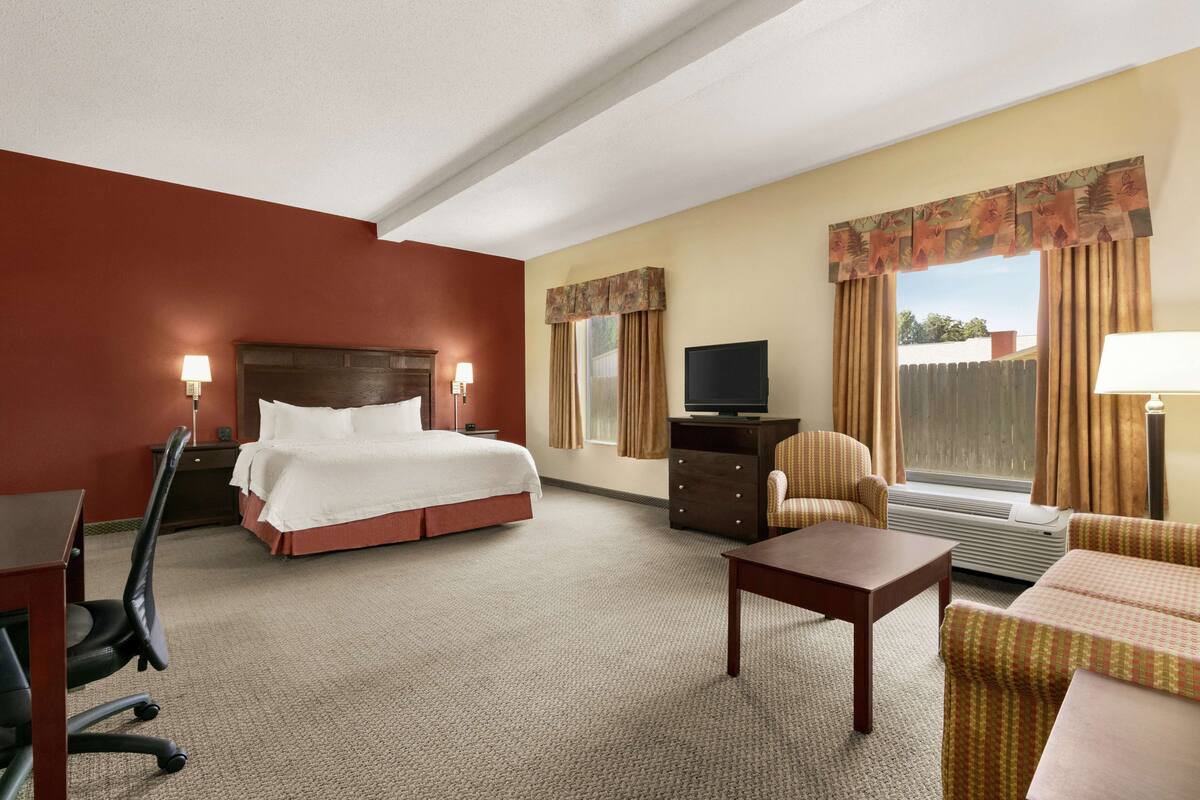 A hotel room with a bed, a desk, a chair, a TV, and a window with curtains.