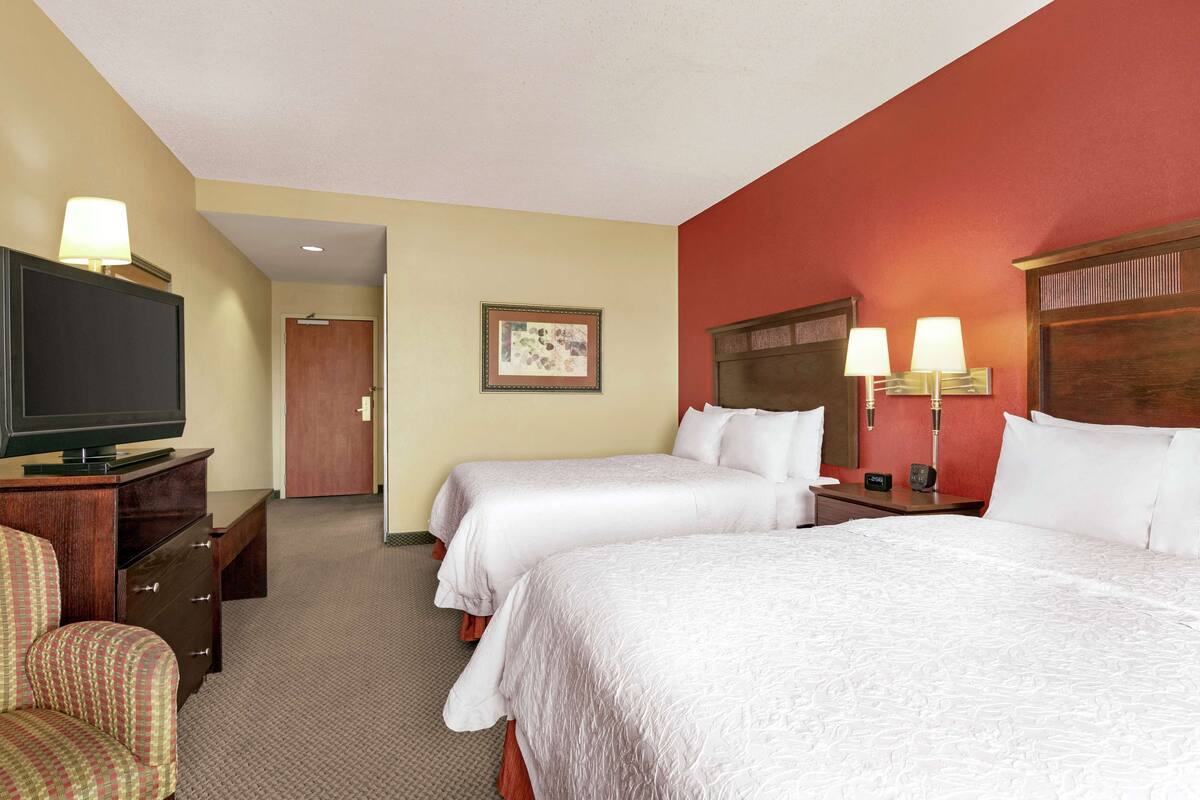 A hotel room with two beds, a TV, a desk, and a chair.