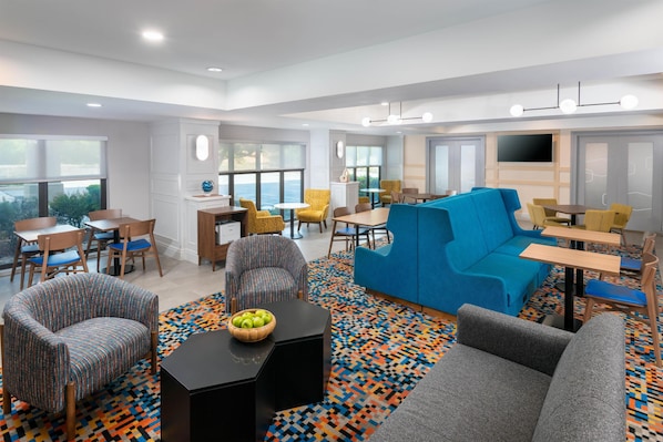 A modern hotel room with a blue sofa, grey armchairs, a black coffee table, and a patterned rug.