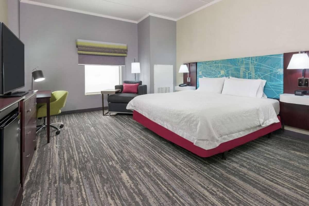 A hotel room with a large bed, a desk with a chair, a television, and a window with blinds.
