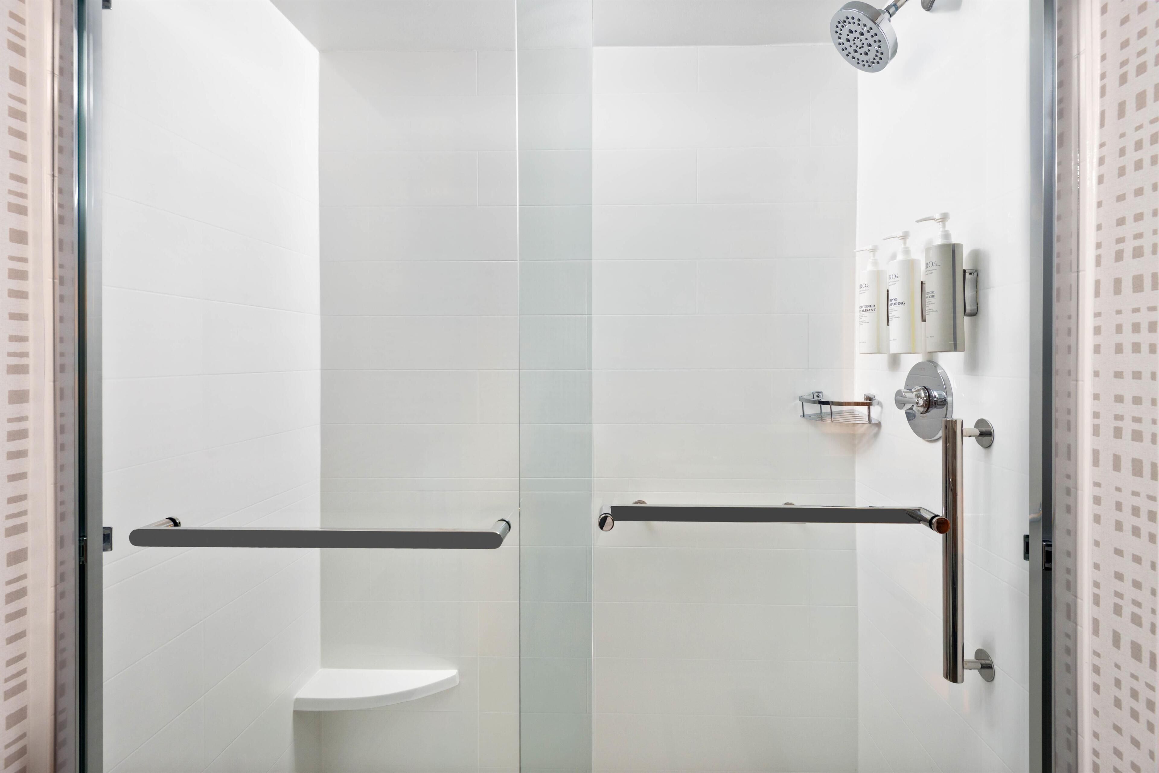 Un baño moderno con azulejos blancos, cabina de ducha de cristal y un inodoro con barra de apoyo.
