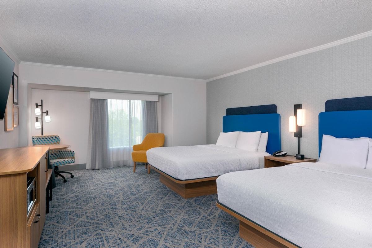 A hotel room with two beds, a desk, a chair, and a window with curtains.