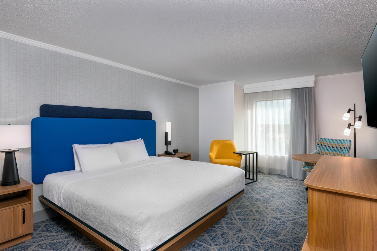 A hotel room with a large bed, a desk, a chair, and a small table.