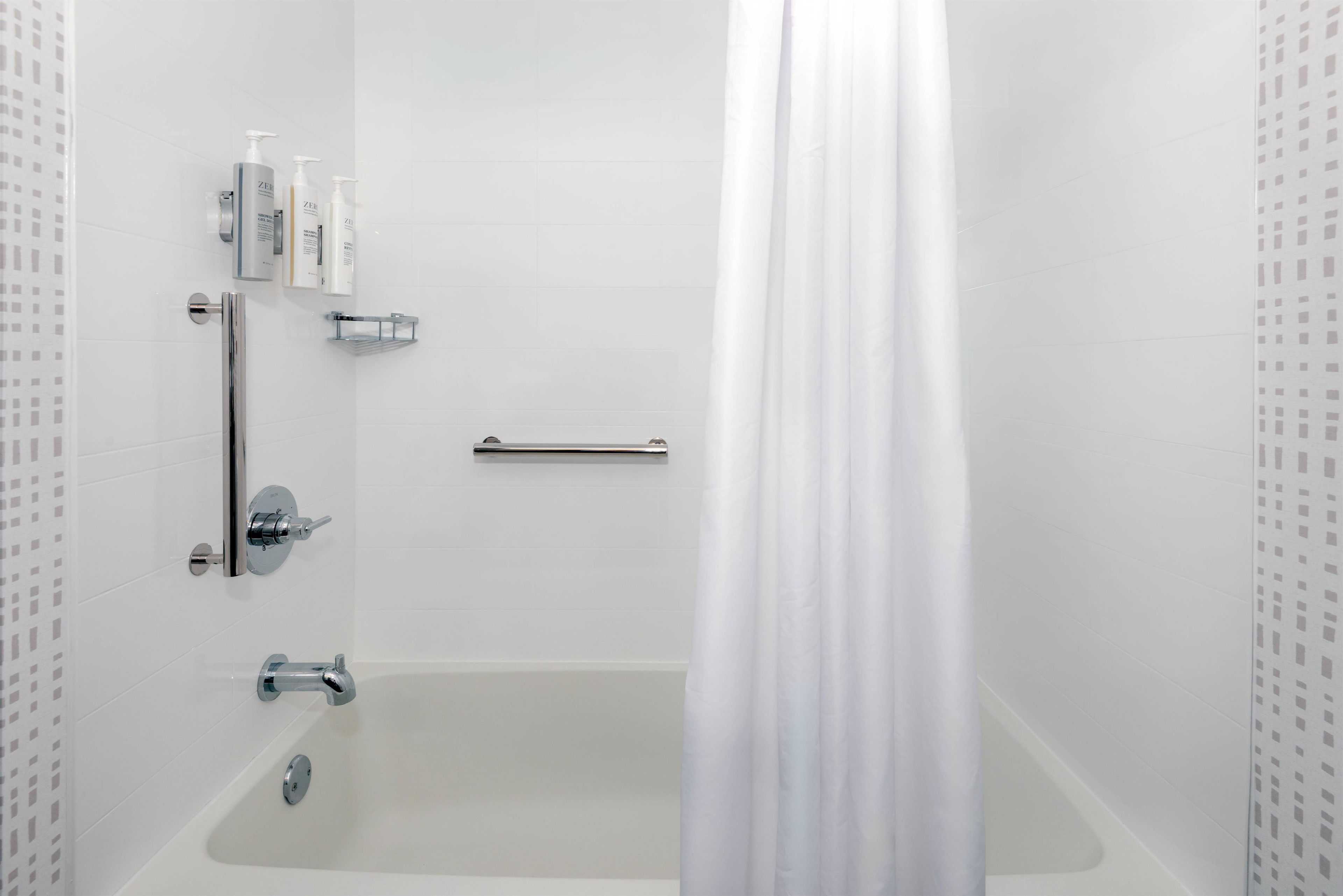 A modern bathroom with a bathtub, shower, and handrails.