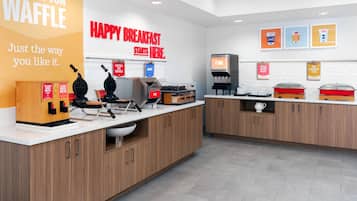 A clean, modern breakfast area with waffle makers, a coffee station, and a sign reading 'HAPPY BREAKFAST STARTS HERE.'