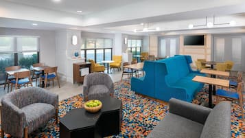 A modern hotel room with a blue sofa, grey armchairs, a black coffee table, and a patterned rug.