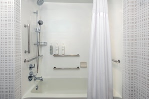 A modern bathroom with a bathtub, shower, and handrails.