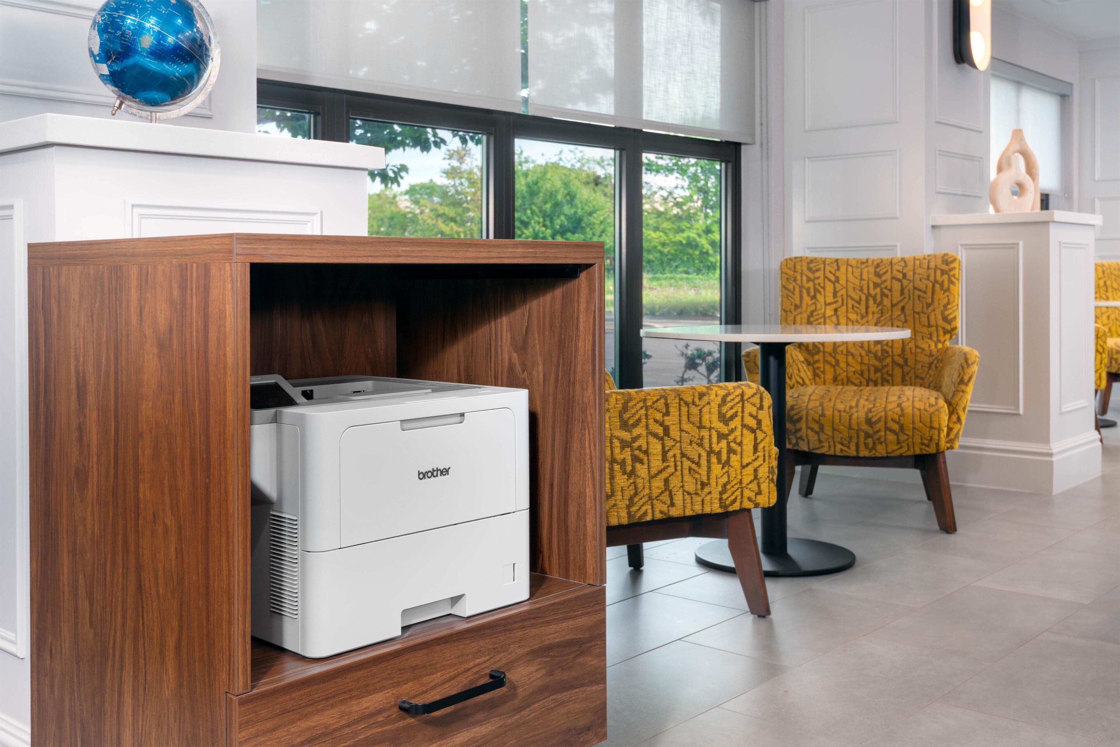 A room with a printer in a wooden cabinet, a yellow patterned chair, and a view through large windows.