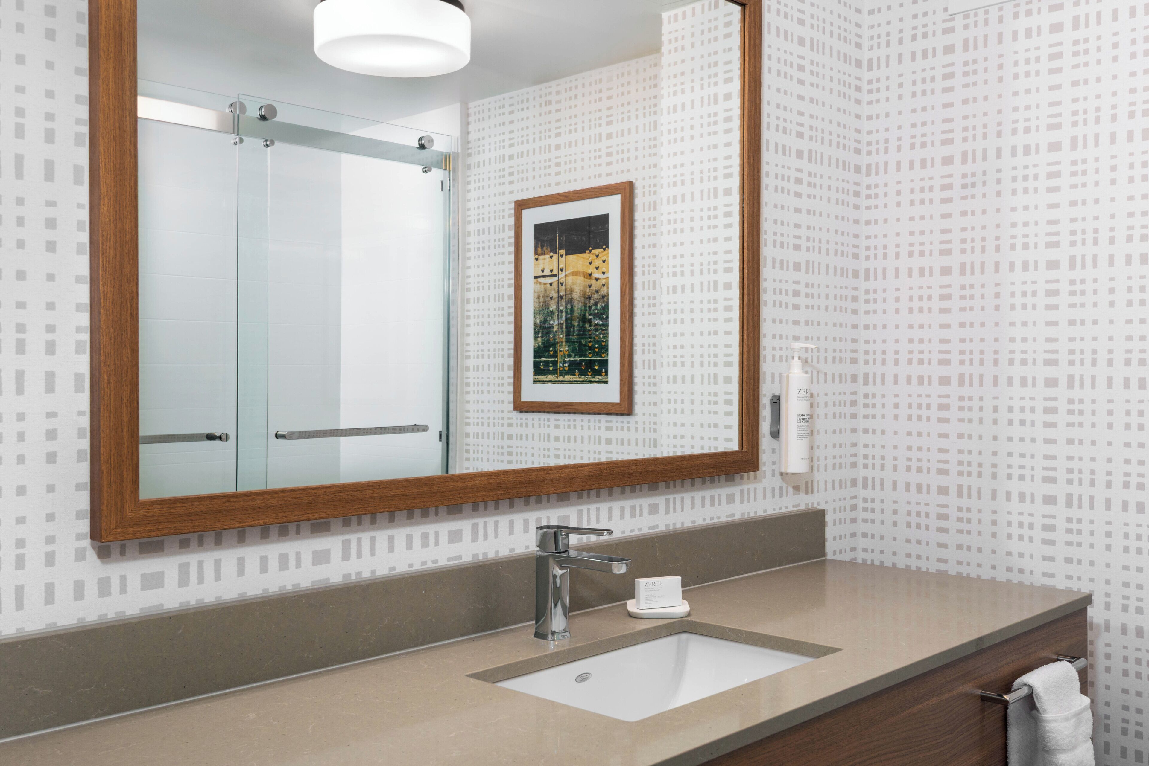 Un bagno con uno specchio grande, un lavandino, un quadro incorniciato e un portascopevoli.