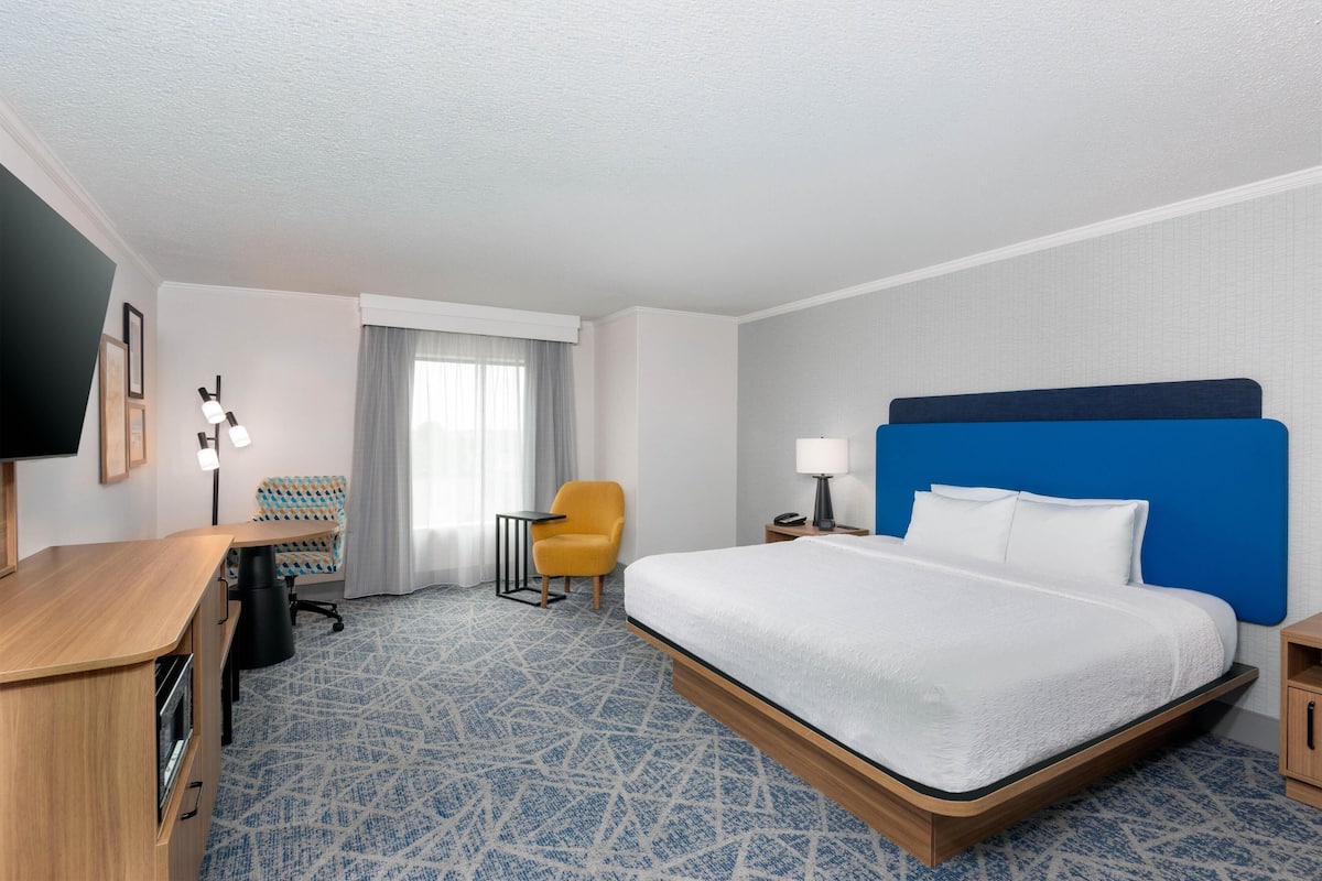 A hotel room with a bed, a desk, a chair, a TV, and a window with curtains.