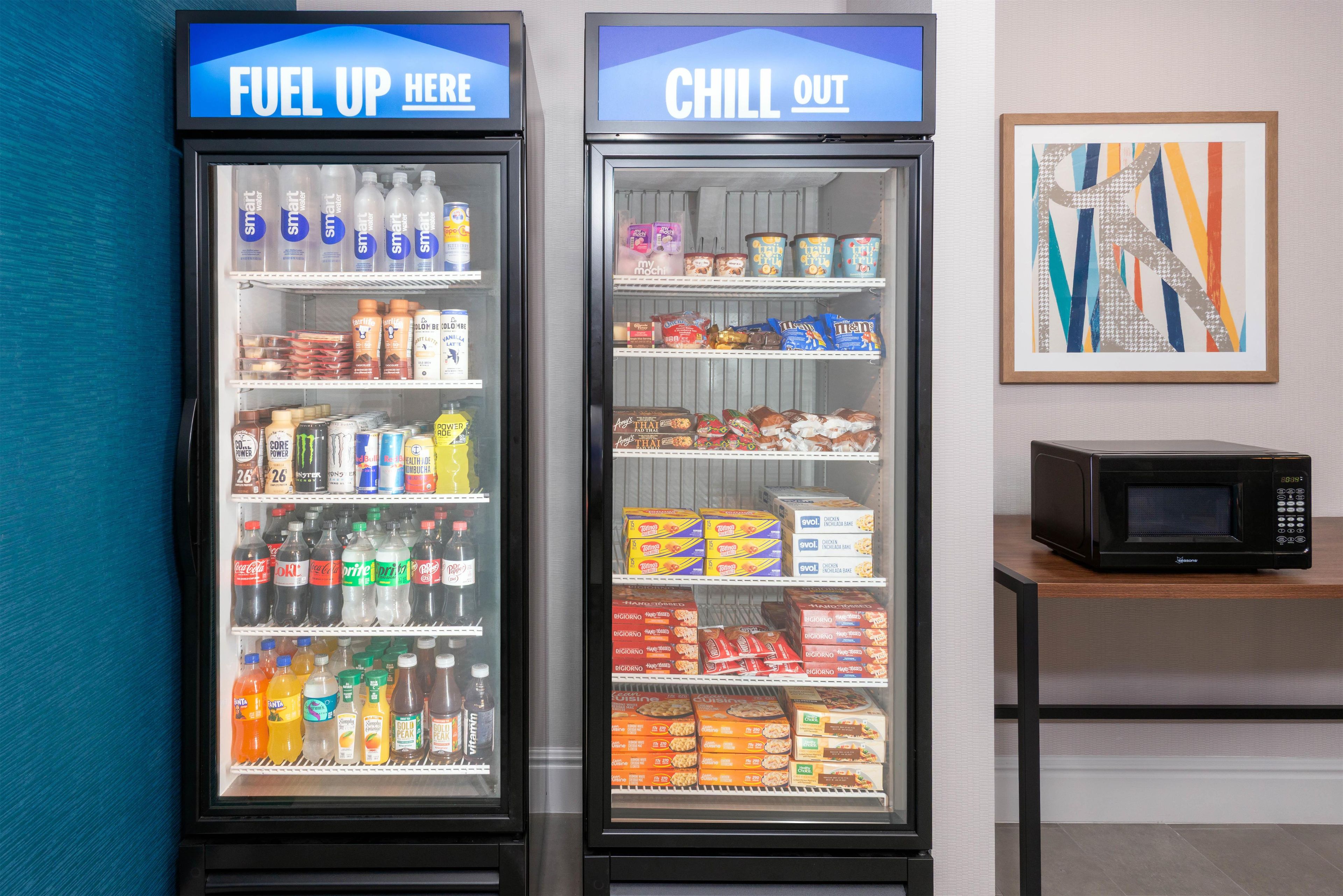 Two beverage vending machines labeled 'Fuel Up Here' and 'Chill Out,' with a microwave on a shelf to the right.