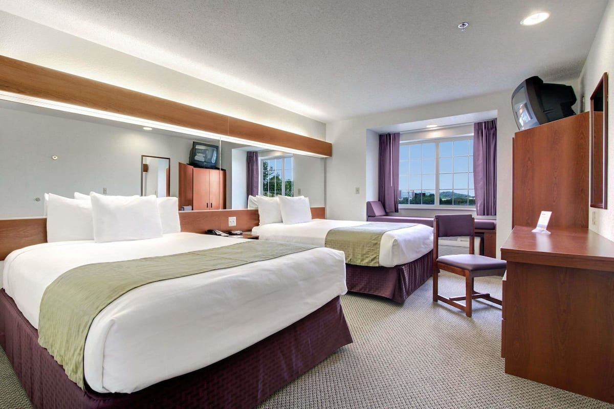 A hotel room with two beds, a desk, a chair, and a television on a wooden cabinet.