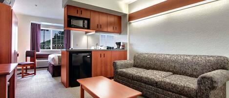 A compact living space with a kitchenette, a sofa, a small table, and a window with curtains.