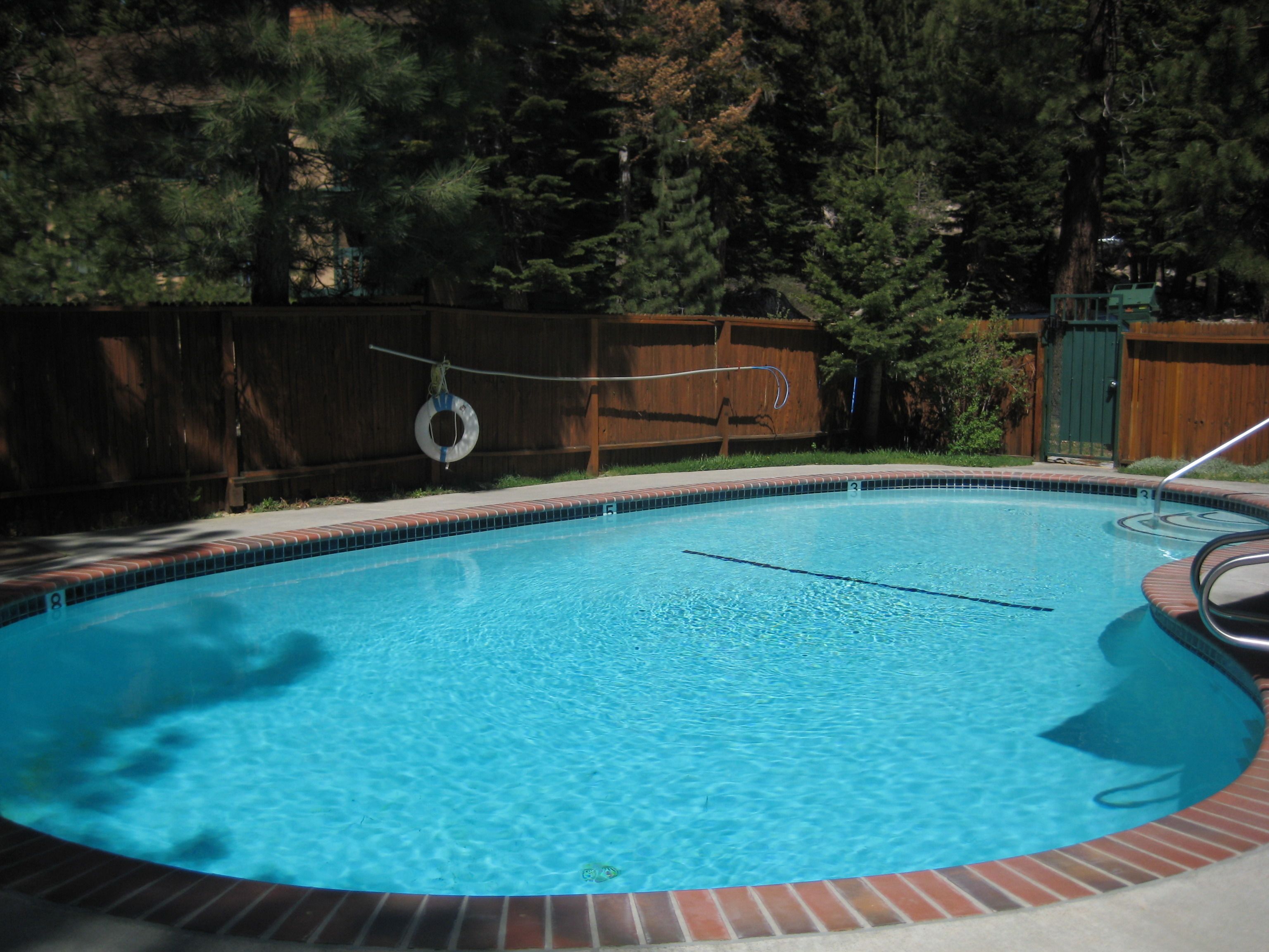 A swimming pool with a wooden deck and a wooden fence in the background.
