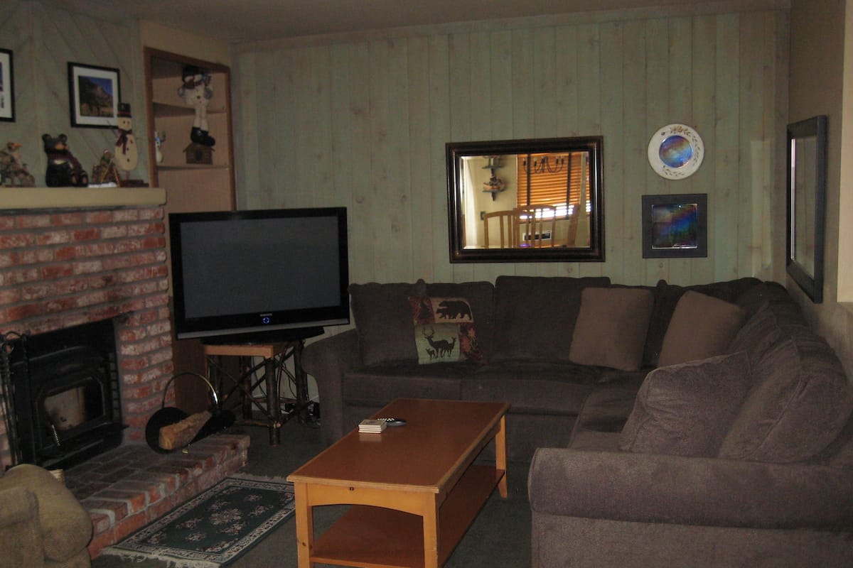 Uma sala de estar com lareira de tijolos, televisão, sofá e mesa de centro.