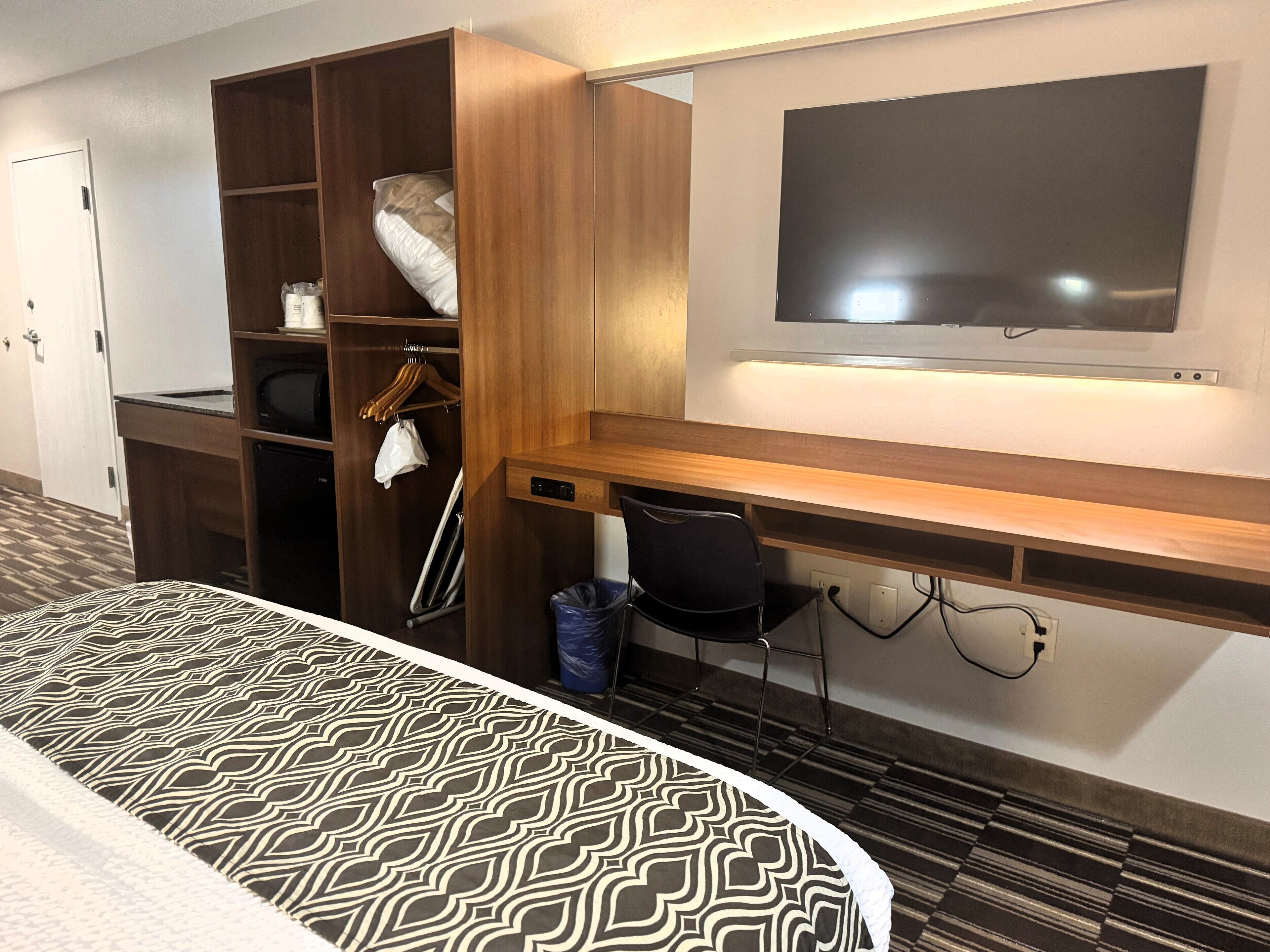 Una habitación de hotel con cama, escritorio, televisor, armario y un cesto de basura.