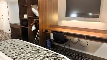 Una habitación de hotel con cama, escritorio, televisor, armario y un cesto de basura.