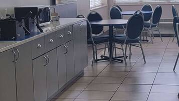 Een nette, moderne keuken met een eettafel en stoelen, een magnetron en een spoelbak.