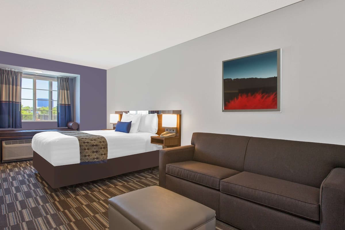 A hotel room with a large bed, a sofa, a small table, and a painting on the wall.