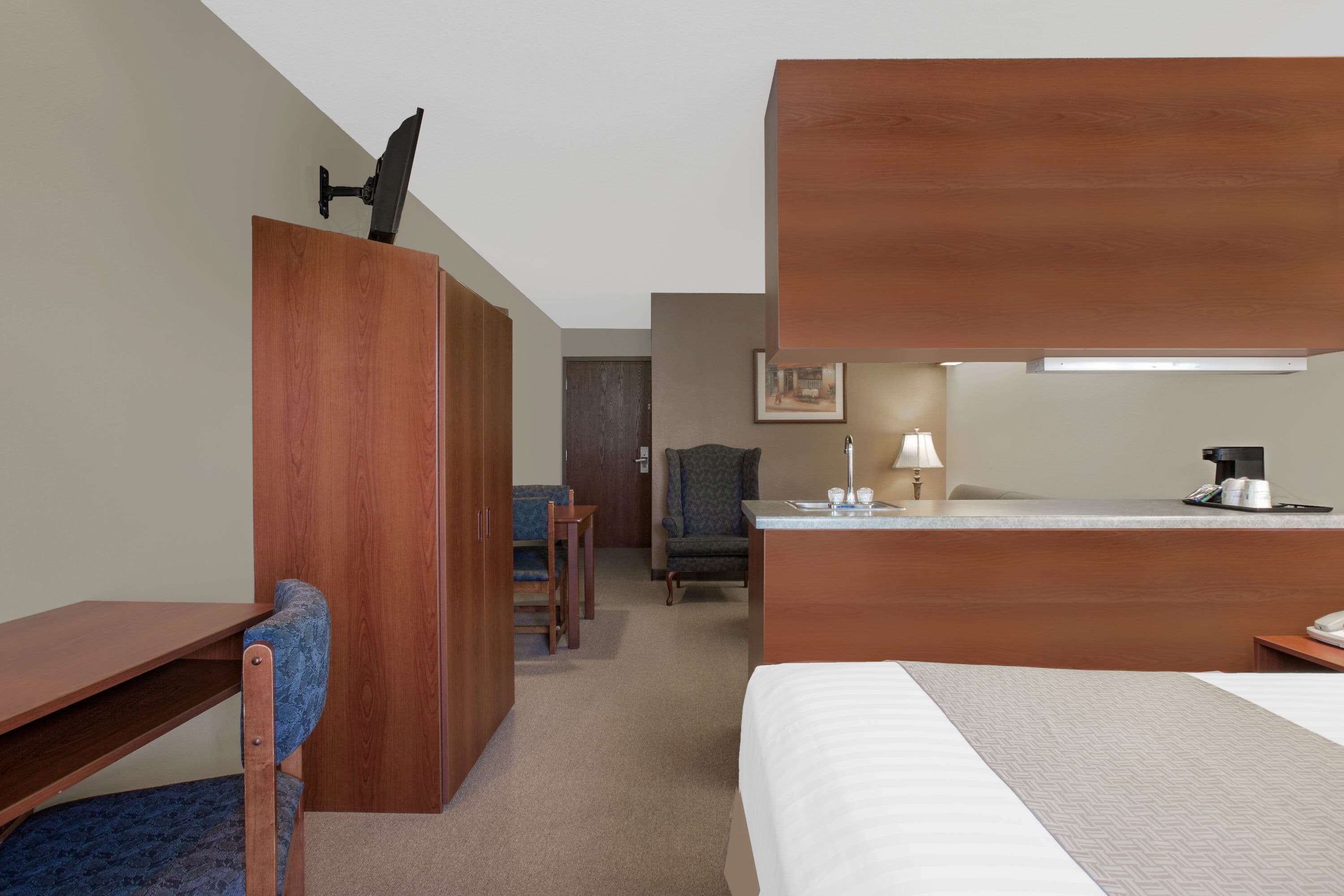 Una habitación de hotel con cama, escritorio, silla, armario y una pequeña cocina.