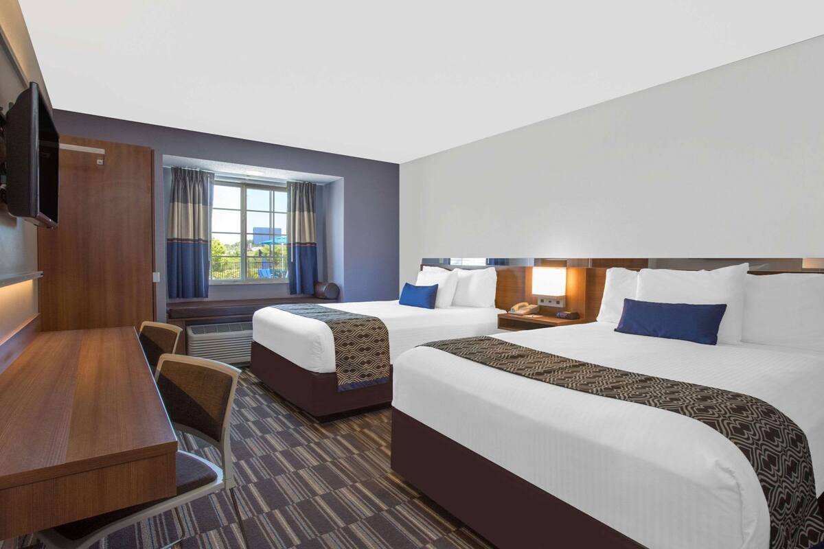 A hotel room with a bed, a desk, a chair, a TV, and a window with curtains.