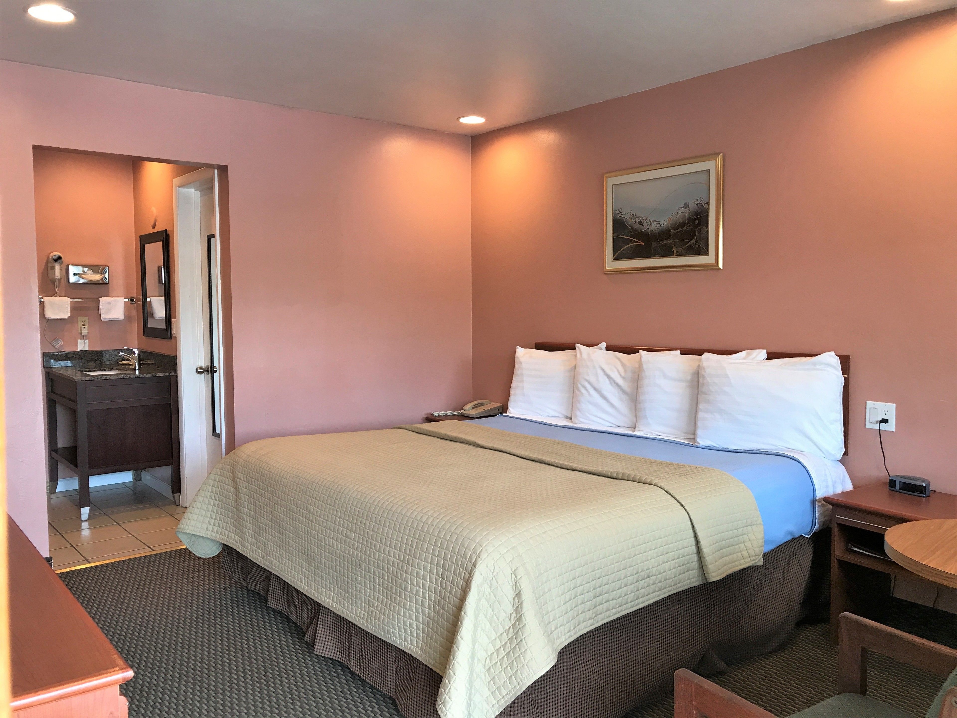 Una camera d'albergo con un letto, un comodino e un bagno visibile attraverso una porta aperta.