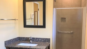 A bathroom with a granite countertop sink, a dark wooden vanity, a mirror, and a glass shower enclosure. - Bestway Inn (Grants Pass)