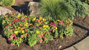A Bestway Inn with a covered front porch, a parking lot, and a landscaped garden with colorful flowers. - Bestway Inn (Grants Pass)