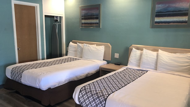 A hotel room with two beds, a wooden floor, a door, and a painting on the wall. - Bestway Inn (Grants Pass)