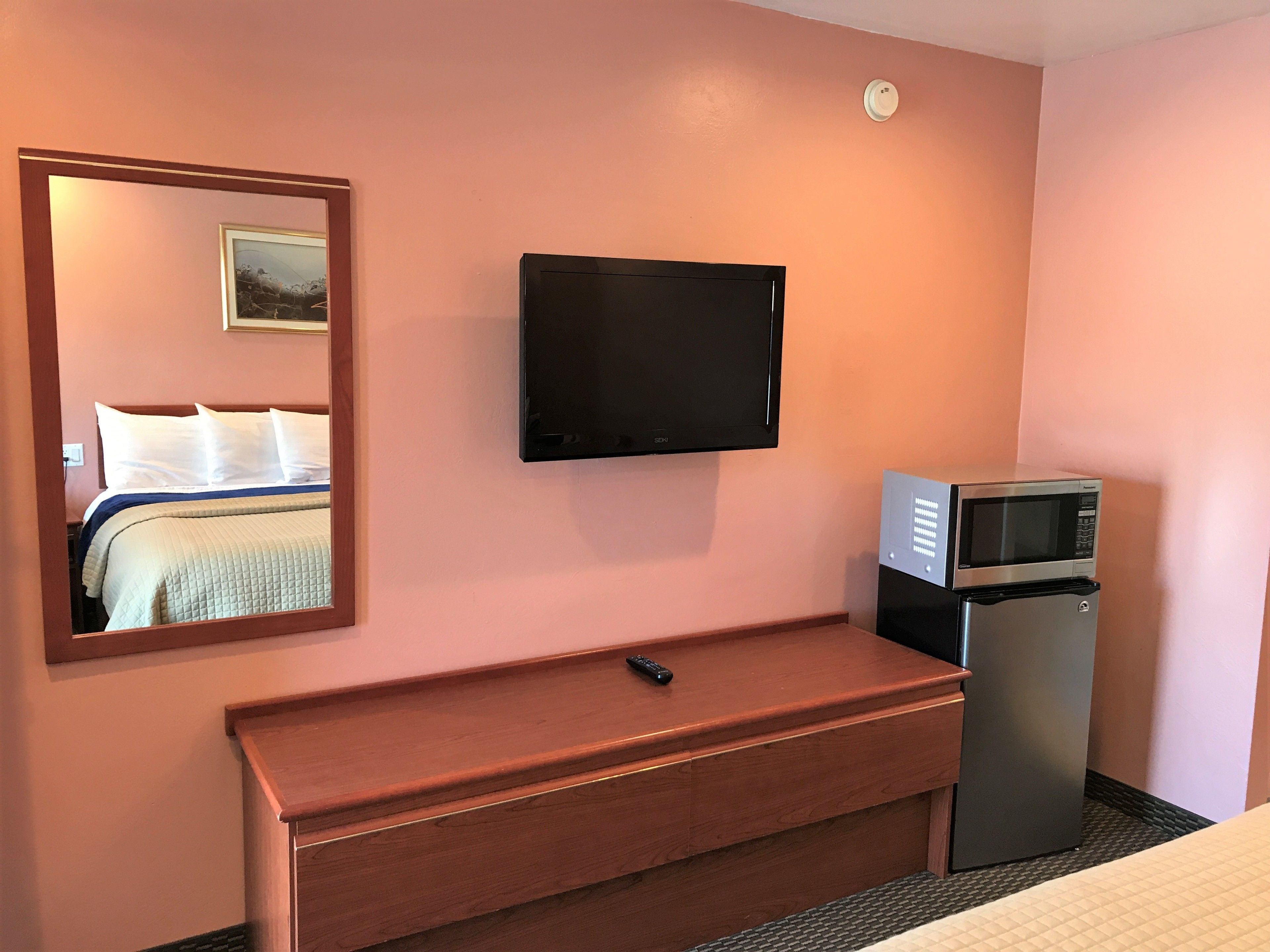 Een hotelkamer met een bed, een aan de muur bevestigde televisie, een magnetron en een houten dressoir.