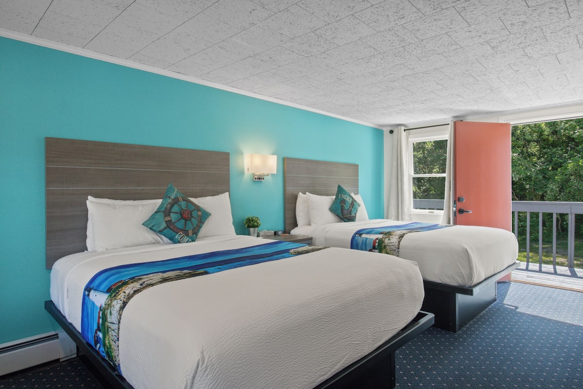 A hotel room with two beds, a view of the outdoors, and a balcony.