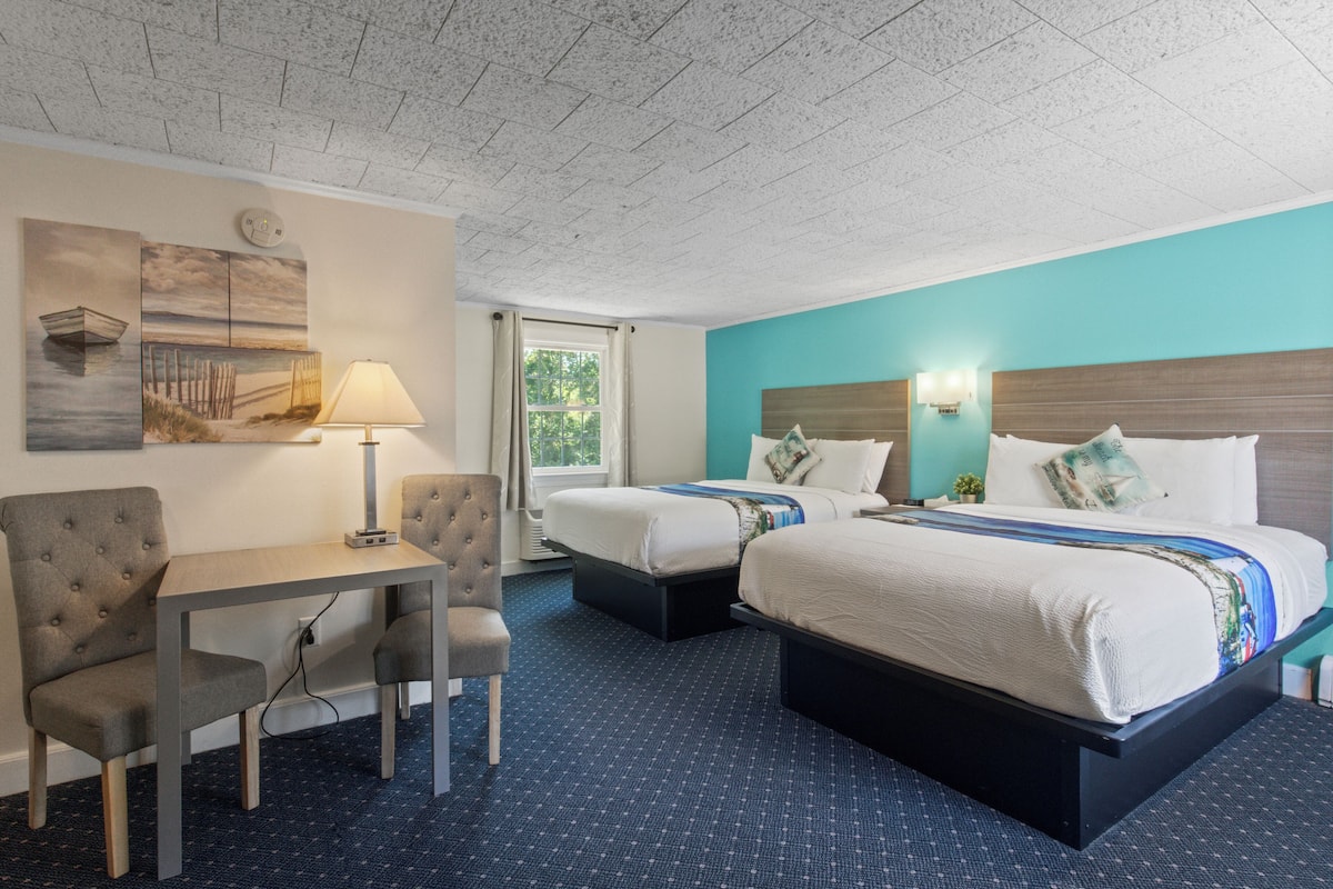 A hotel room with a bed, two bedside tables, a desk with a chair, a lamp, and a window.