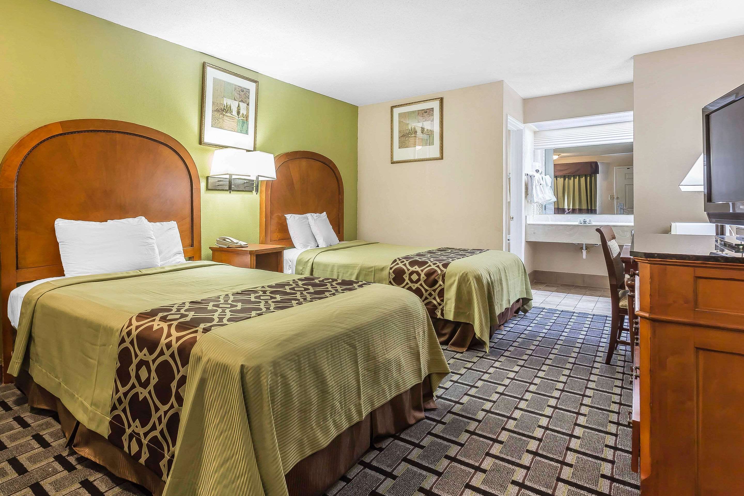 A hotel room with two beds, a desk, a television, and a bathroom visible through an open door.