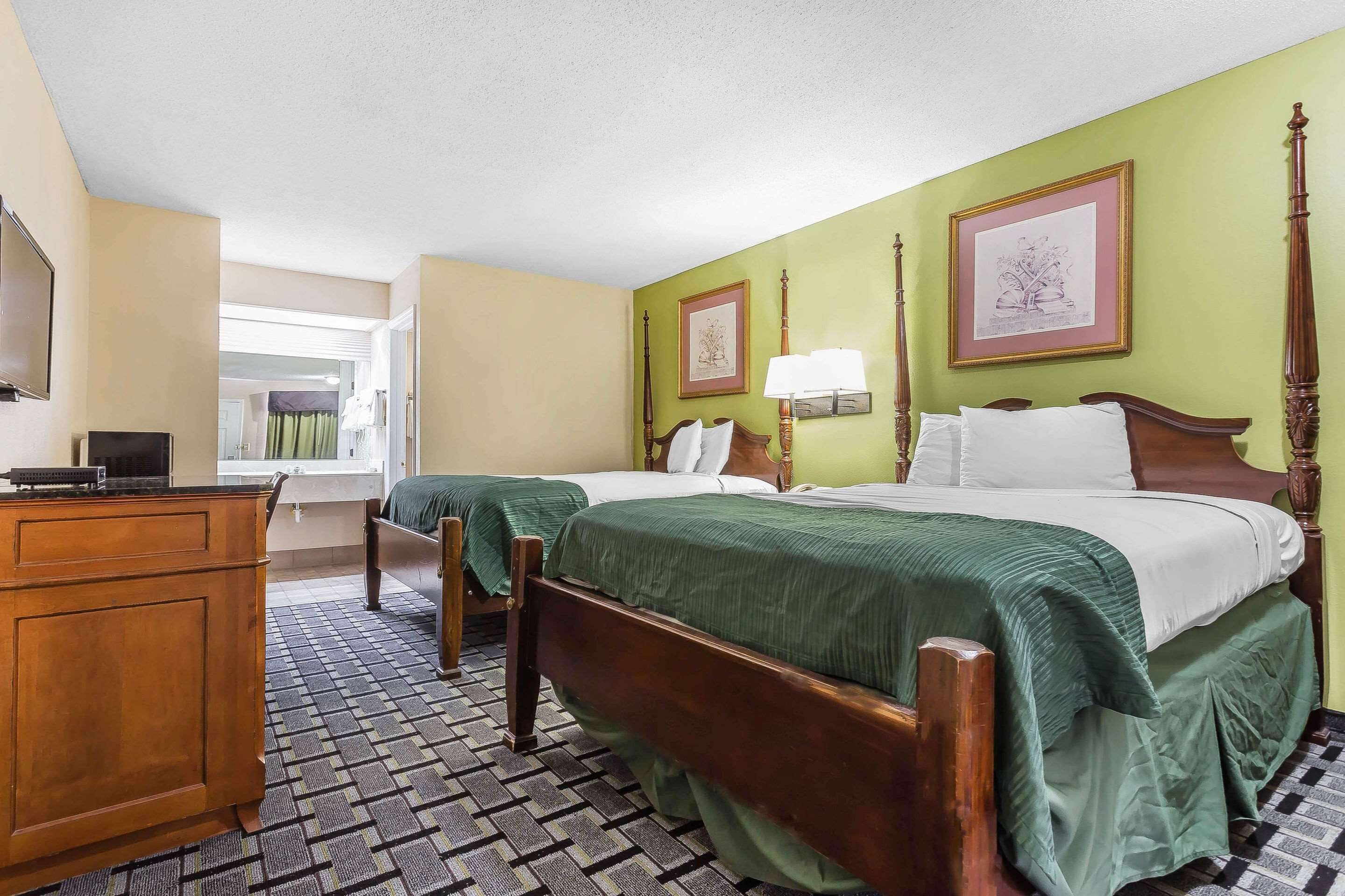 A hotel room with two beds, a wooden dresser, a desk with a computer, and a window with curtains.
