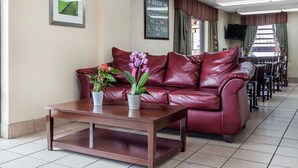 A red leather sofa with a coffee table and potted plants, a television, and a dining area with chairs and tables. - Rodeway Inn Augusta South (Augusta)