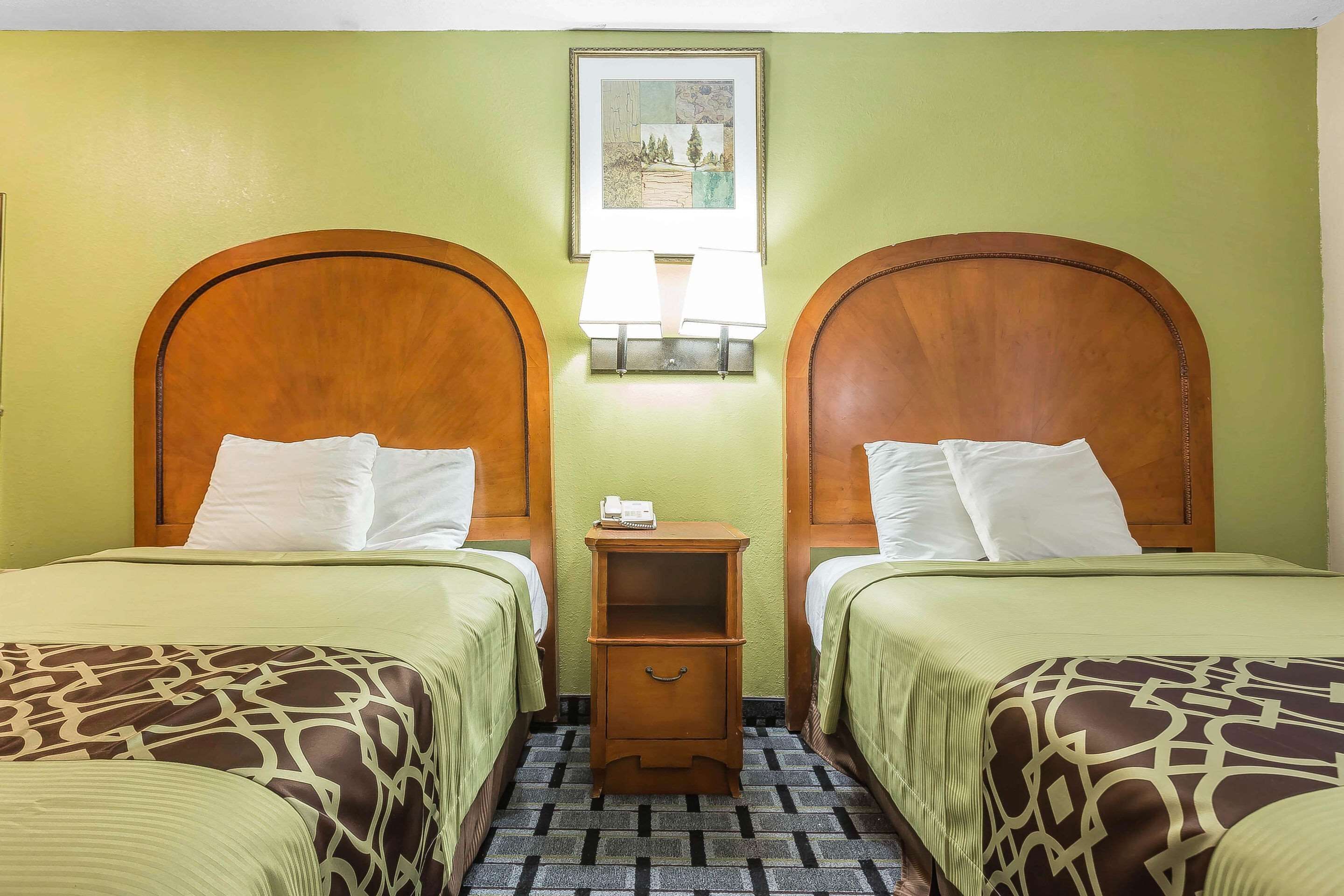 A hotel room with two beds, each with a wooden headboard, a nightstand, and a wall-mounted lamp.