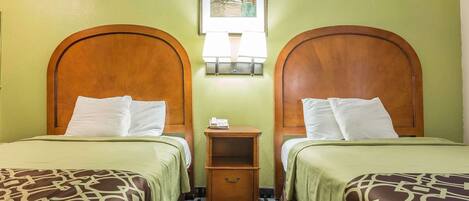 A hotel room with two beds, each with a wooden headboard, a nightstand, and a wall-mounted lamp.