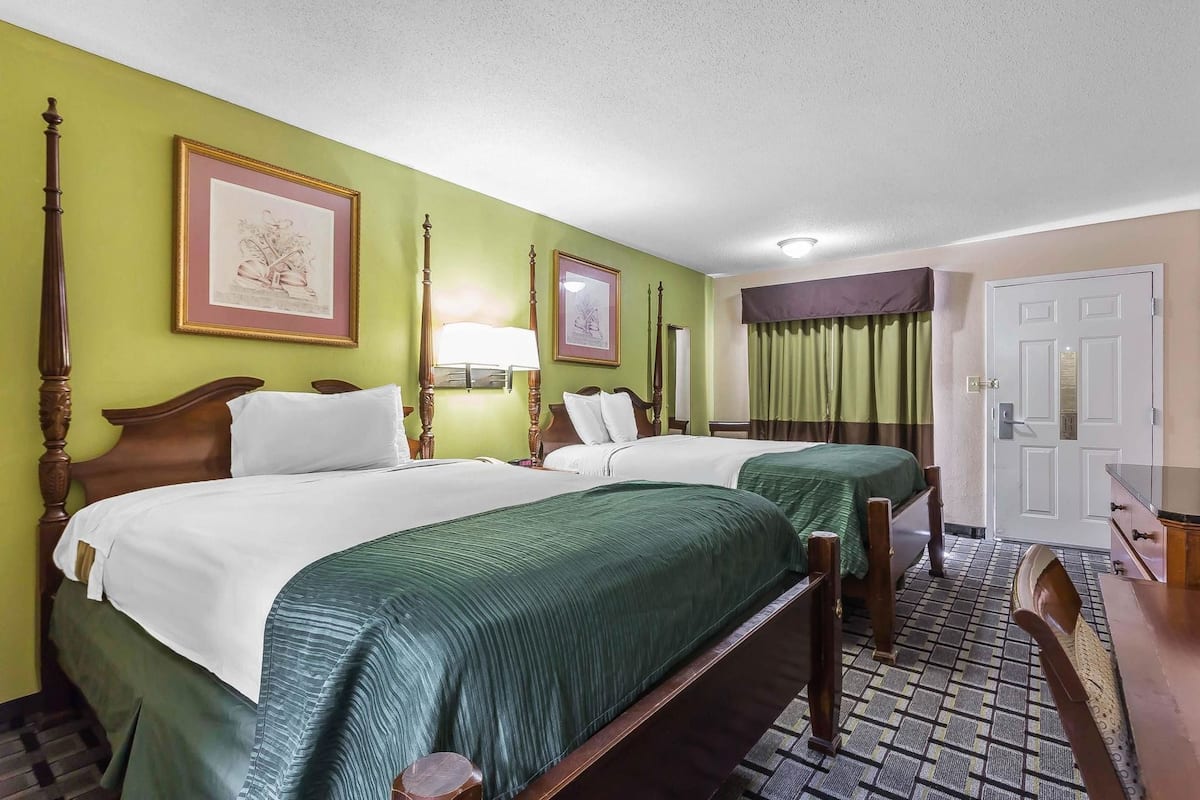 A hotel room with two beds, a desk, and a door.