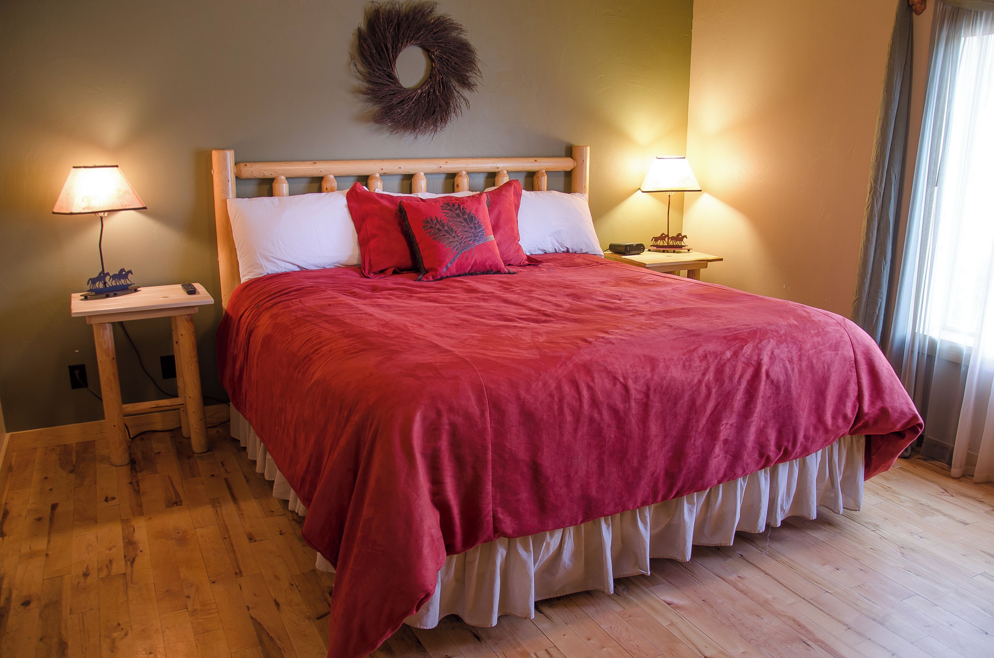 A bed with a wooden headboard, red bedding, two bedside lamps, and a wooden floor.