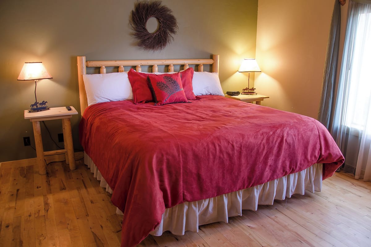 A bed with a wooden headboard, red bedding, two bedside lamps, and a wooden floor.