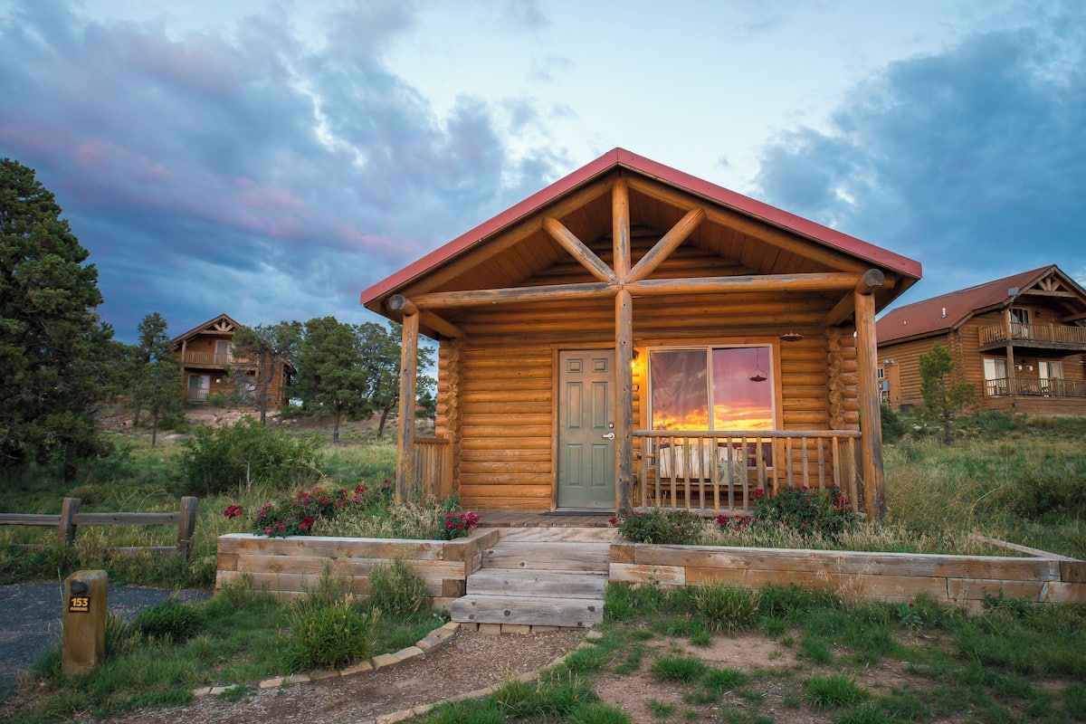 A log cabin with a porch, a wooden door, and a view of the sunset.